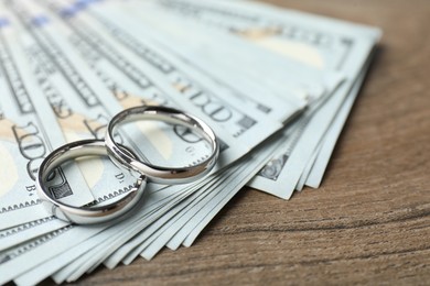 Photo of Silver wedding rings and dollar banknotes on wooden table, closeup