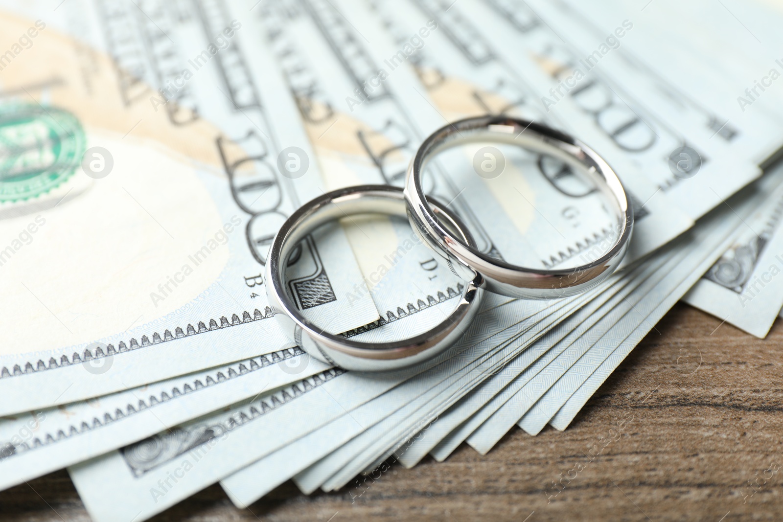Photo of Silver wedding rings and dollar banknotes on wooden table, closeup