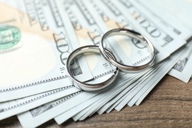 Photo of Silver wedding rings and dollar banknotes on wooden table, closeup