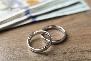 Photo of Silver wedding rings and dollar banknotes on wooden table, closeup