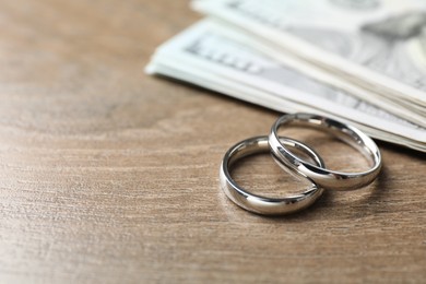 Photo of Silver wedding rings and dollar banknotes on wooden table, closeup. Space for text