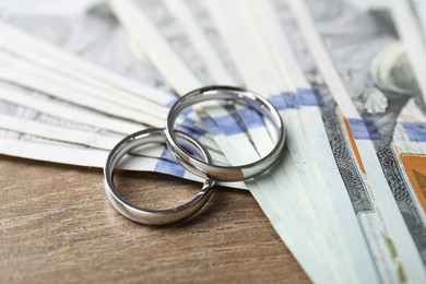 Photo of Silver wedding rings and dollar banknotes on wooden table, closeup