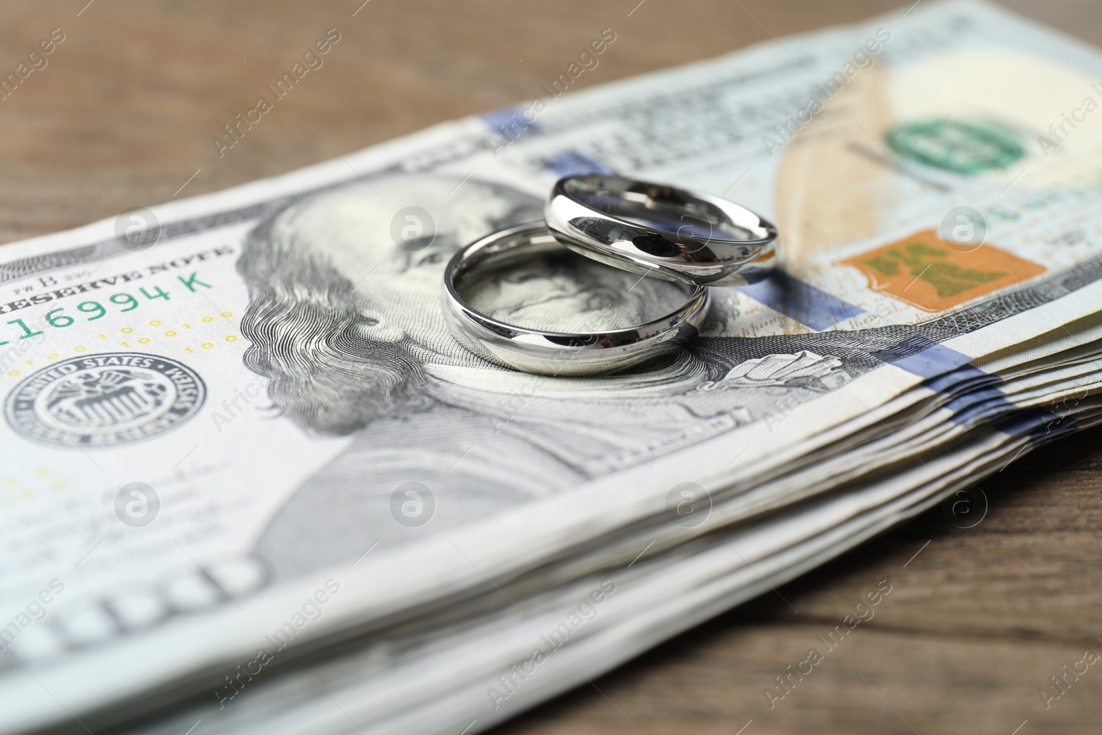 Photo of Silver wedding rings and dollar banknotes on wooden table, closeup