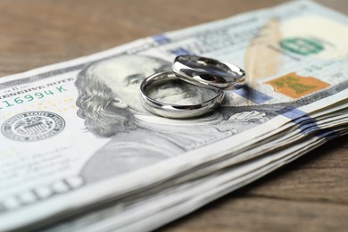 Photo of Silver wedding rings and dollar banknotes on wooden table, closeup