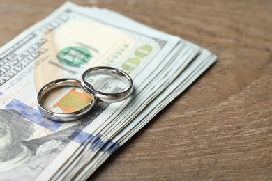 Photo of Silver wedding rings and dollar banknotes on wooden table, closeup. Space for text