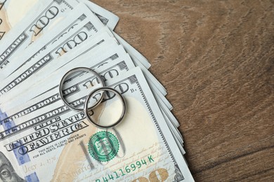 Photo of Silver wedding rings and dollar banknotes on wooden table, flat lay. Space for text