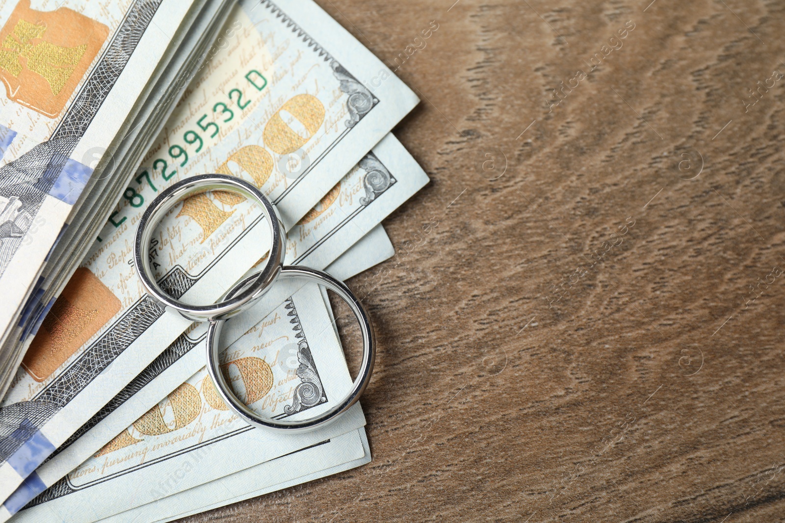 Photo of Silver wedding rings and dollar banknotes on wooden table, flat lay. Space for text
