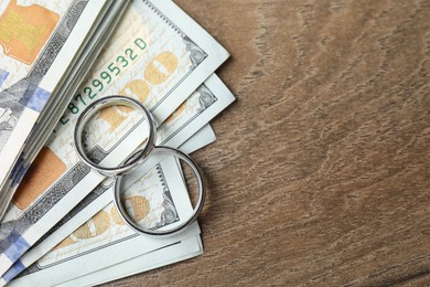 Photo of Silver wedding rings and dollar banknotes on wooden table, flat lay. Space for text