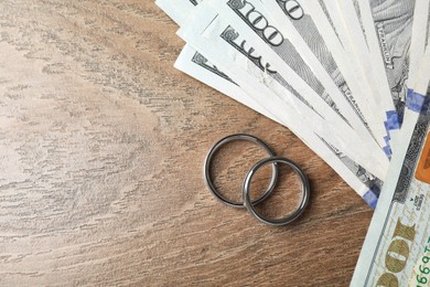 Photo of Silver wedding rings and dollar banknotes on wooden table, flat lay. Space for text