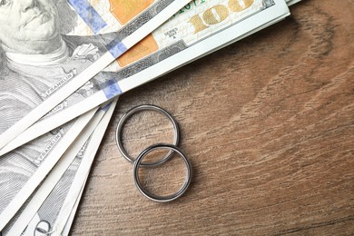 Photo of Silver wedding rings and dollar banknotes on wooden table, flat lay. Space for text