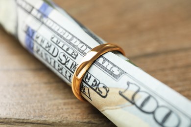 Photo of Gold ring and dollar banknotes on wooden table, closeup