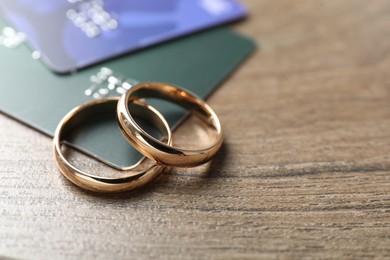 Photo of Gold wedding rings and credit cards on wooden table, closeup. Space for text