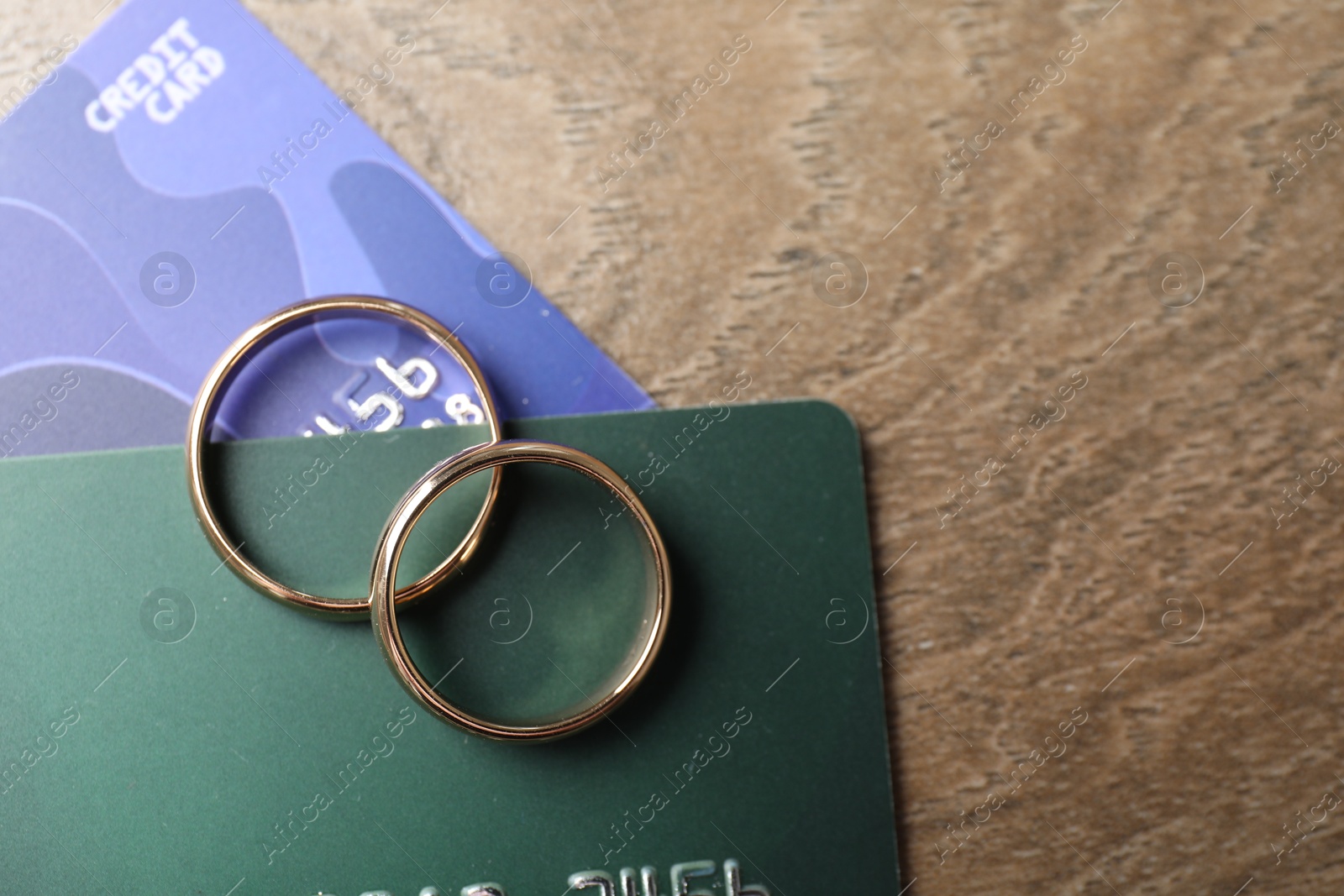 Photo of Gold wedding rings and credit cards on wooden table, flat lay. Space for text