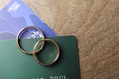 Photo of Gold wedding rings and credit cards on wooden table, flat lay. Space for text