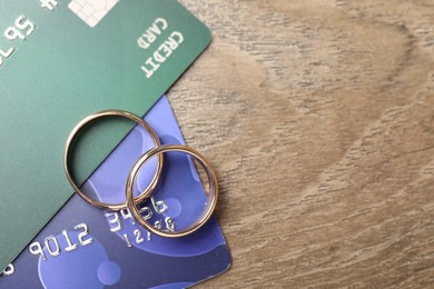 Photo of Gold wedding rings and credit cards on wooden table, flat lay. Space for text