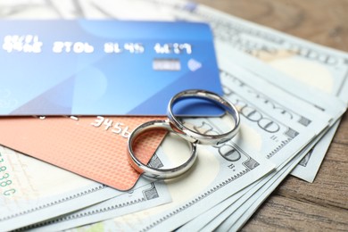 Photo of Silver wedding rings, dollar banknotes and credit cards on wooden table, closeup
