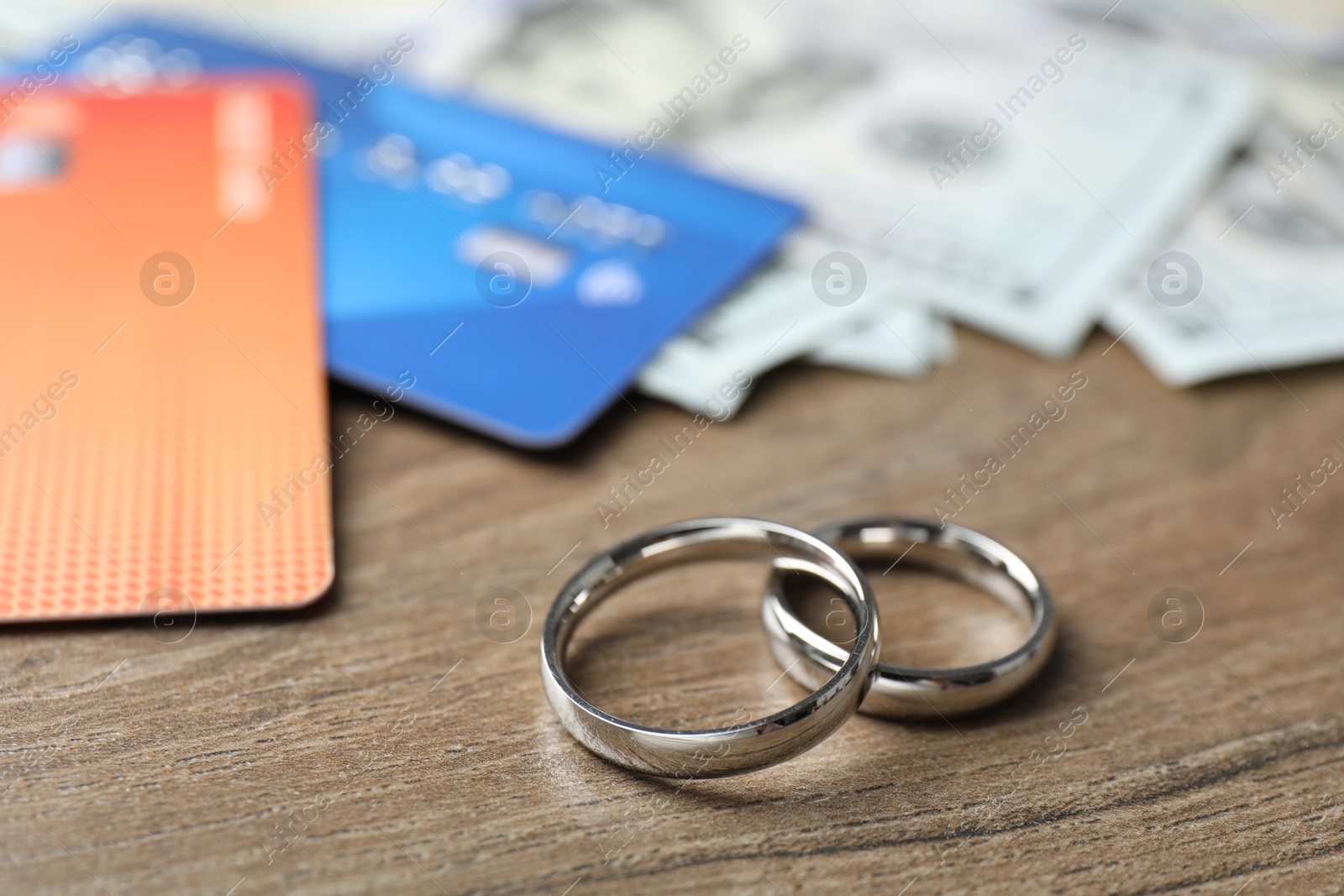 Photo of Silver wedding rings, dollar banknotes and credit cards on wooden table, closeup