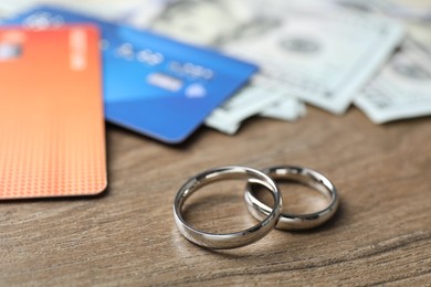 Photo of Silver wedding rings, dollar banknotes and credit cards on wooden table, closeup