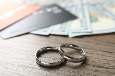 Photo of Silver wedding rings, dollar banknotes and credit cards on wooden table, closeup