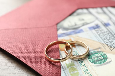 Photo of Gold wedding rings, envelope and dollar banknotes on wooden table, closeup