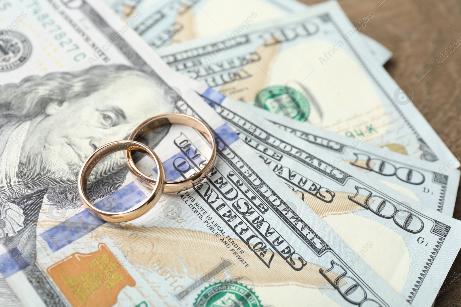 Photo of Gold wedding rings and dollar banknotes on wooden table, closeup