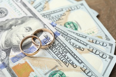 Photo of Gold wedding rings and dollar banknotes on wooden table, closeup