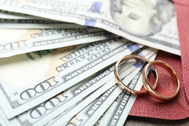 Photo of Gold wedding rings, envelope and dollar banknotes on wooden table, closeup