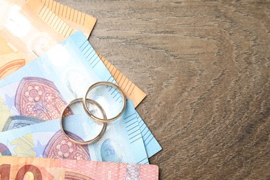 Photo of Gold wedding rings and euro banknotes on wooden table, flat lay. Space for text