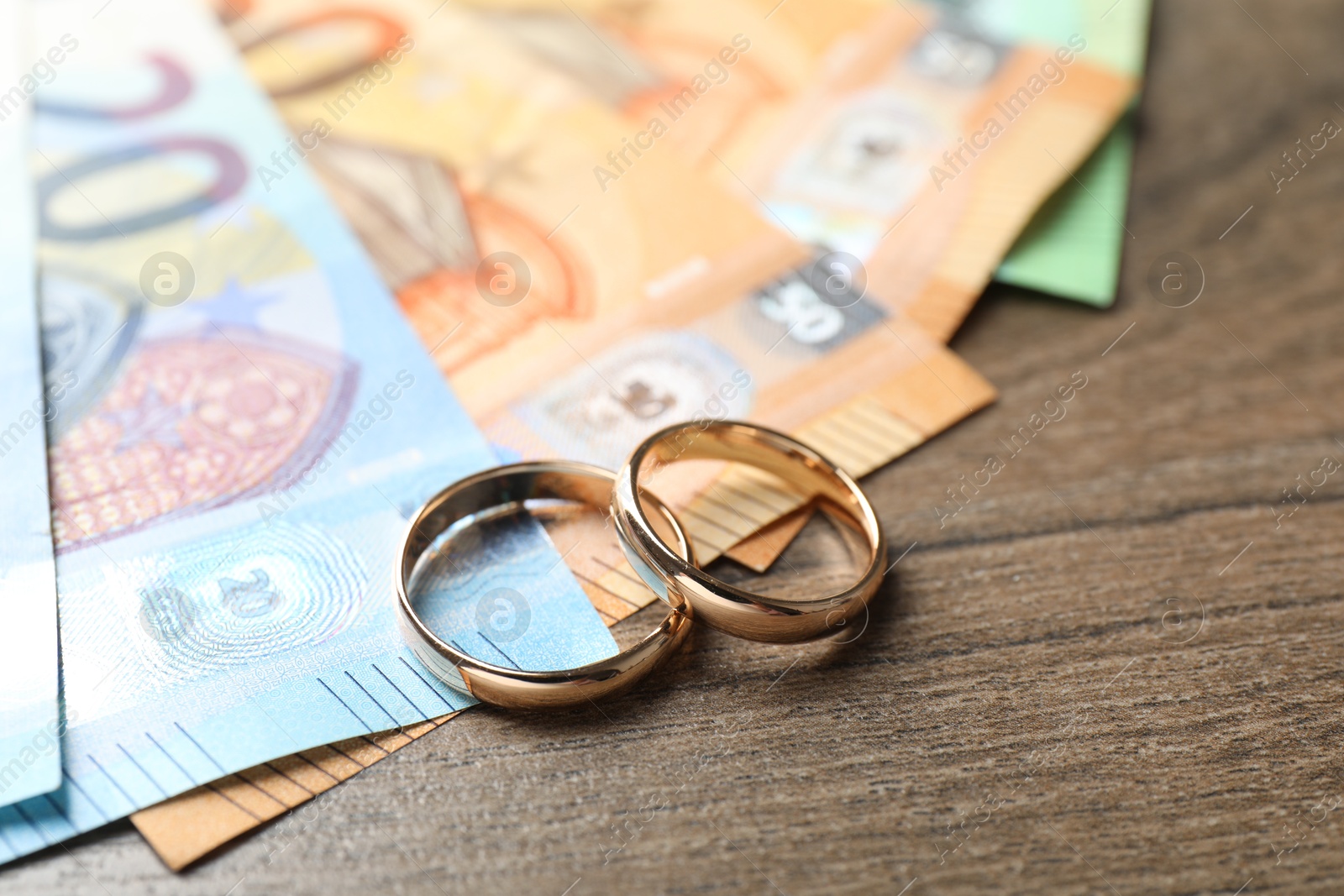 Photo of Gold wedding rings and euro banknotes on wooden table, closeup