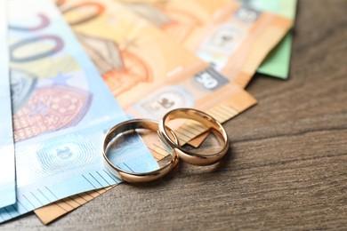 Photo of Gold wedding rings and euro banknotes on wooden table, closeup