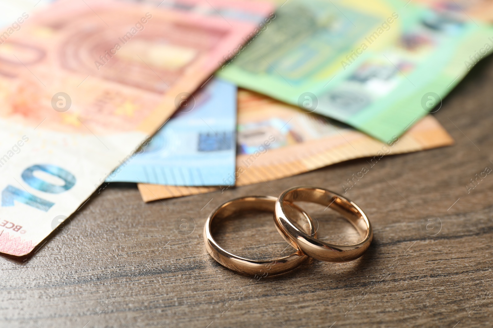 Photo of Gold wedding rings and euro banknotes on wooden table, closeup