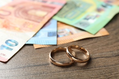 Photo of Gold wedding rings and euro banknotes on wooden table, closeup