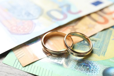 Photo of Gold wedding rings and euro banknotes on wooden table, closeup