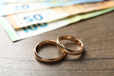 Photo of Gold wedding rings and euro banknotes on wooden table, closeup