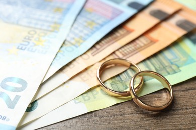 Photo of Gold wedding rings and euro banknotes on wooden table, closeup
