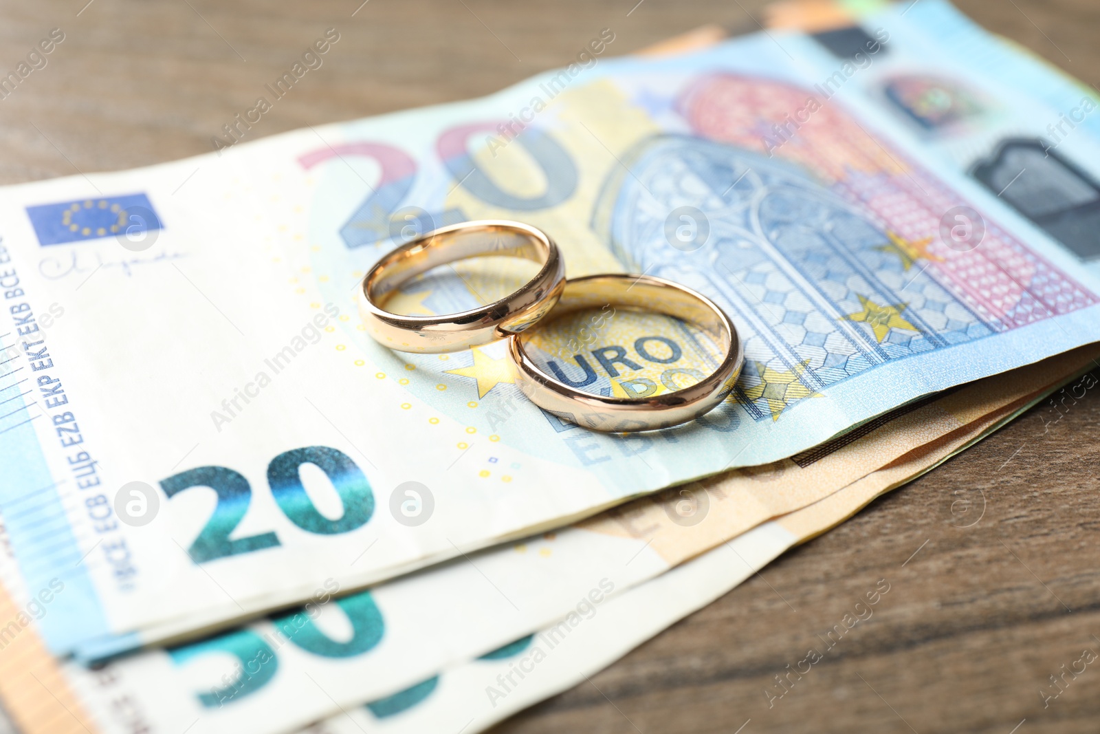 Photo of Gold wedding rings and euro banknotes on wooden table, closeup