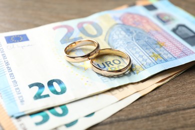 Photo of Gold wedding rings and euro banknotes on wooden table, closeup