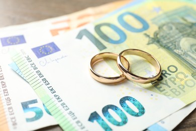 Photo of Gold wedding rings and euro banknotes on wooden table, closeup
