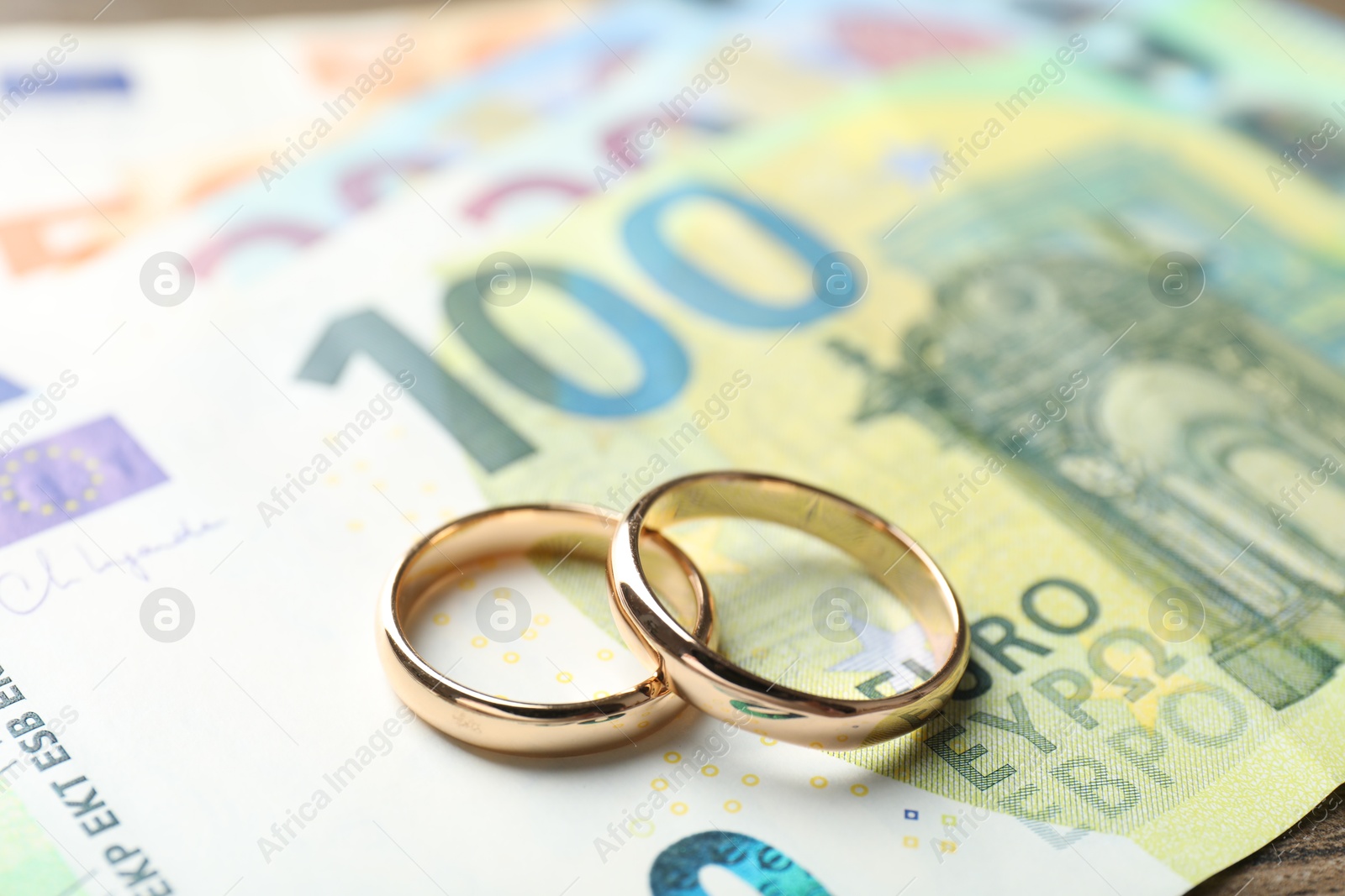 Photo of Gold wedding rings and euro banknotes on wooden table, closeup