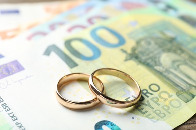 Photo of Gold wedding rings and euro banknotes on wooden table, closeup