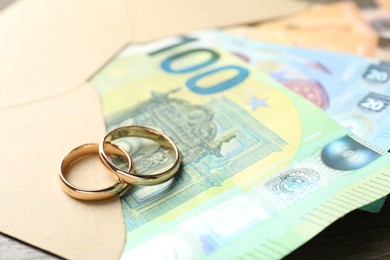 Photo of Gold wedding rings, envelope and euro banknotes on wooden table, closeup