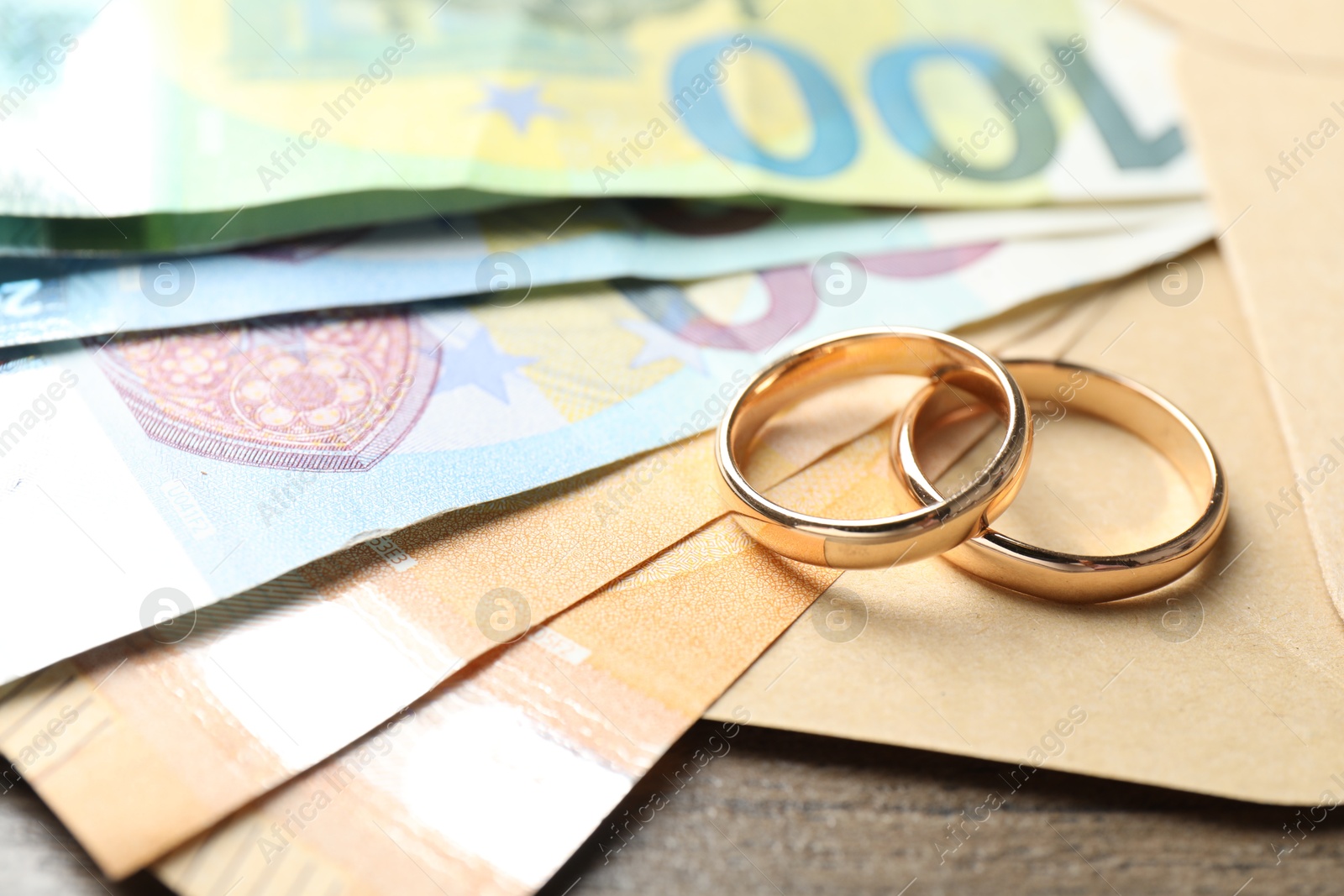 Gold wedding rings, envelope and euro banknotes on wooden table, closeup Photo of Gold wedding rings, envelope and euro banknotes on wooden table, closeup
