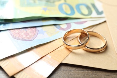 Photo of Gold wedding rings, envelope and euro banknotes on wooden table, closeup
