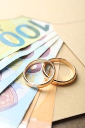 Photo of Gold wedding rings, envelope and euro banknotes on wooden table, closeup