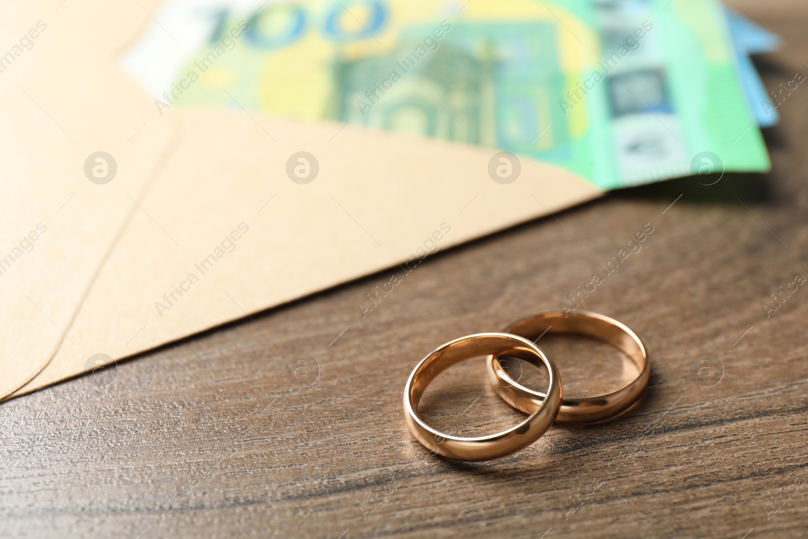 Photo of Gold wedding rings, envelope and euro banknotes on wooden table, closeup