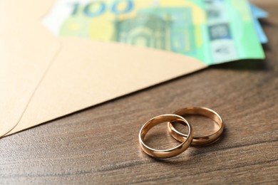 Photo of Gold wedding rings, envelope and euro banknotes on wooden table, closeup