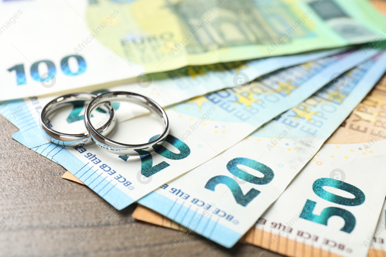 Photo of Silver wedding rings and euro banknotes on wooden table, closeup