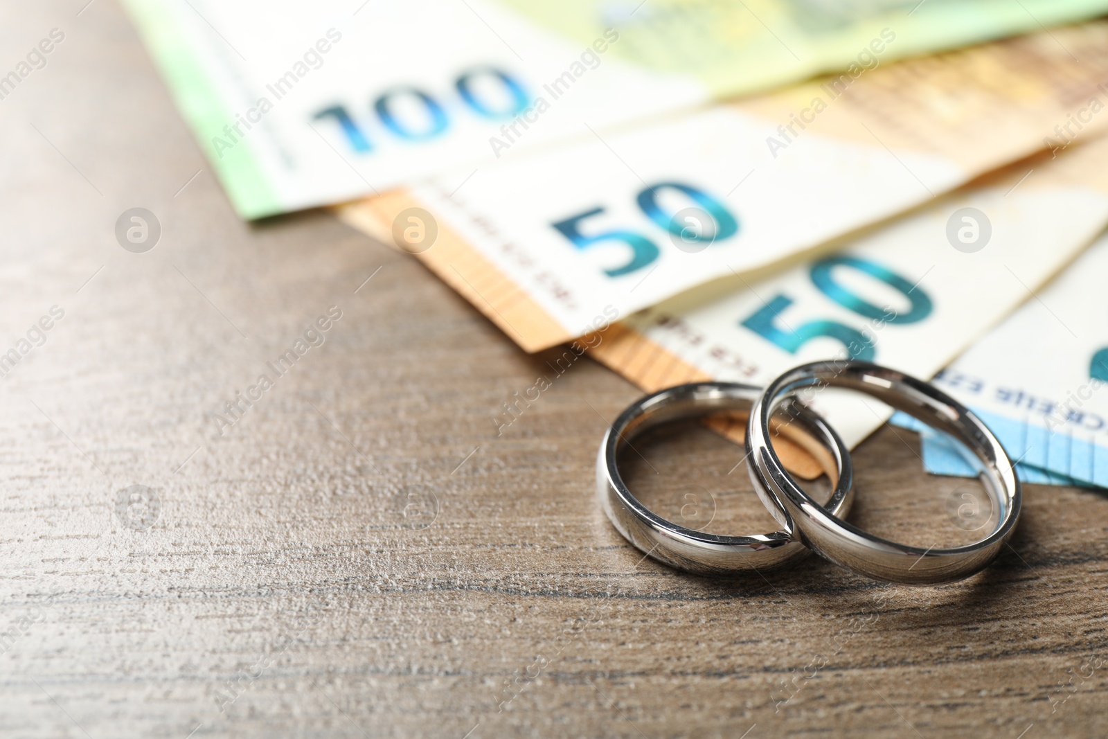 Photo of Silver wedding rings and euro banknotes on wooden table, closeup. Space for text