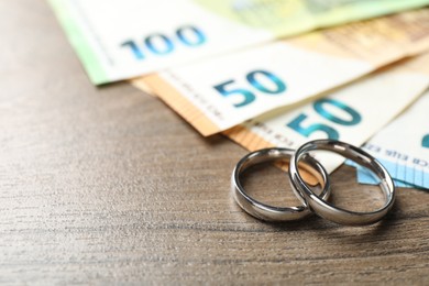 Photo of Silver wedding rings and euro banknotes on wooden table, closeup. Space for text