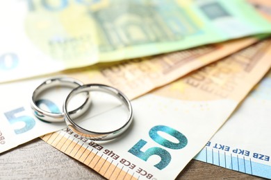 Photo of Silver wedding rings and euro banknotes on wooden table, closeup